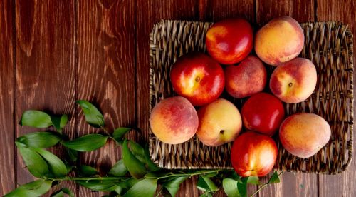 top-view-peaches-basket-plate-wooden-surface-decorated-with-leaves
